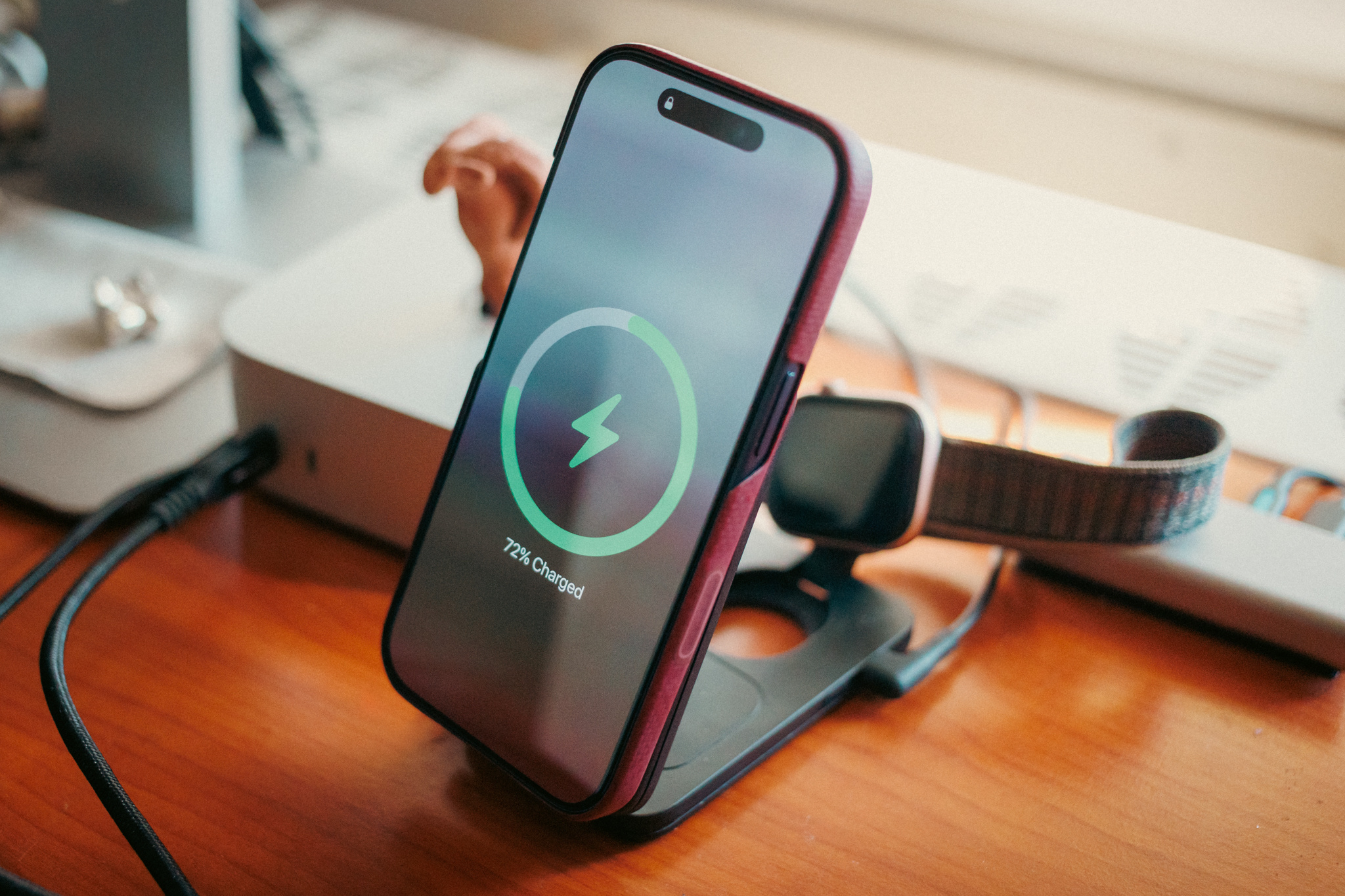 Close-up of an iPhone showing a charging animation on an ESR CryoBoost stand, with an Apple Watch behind it.
